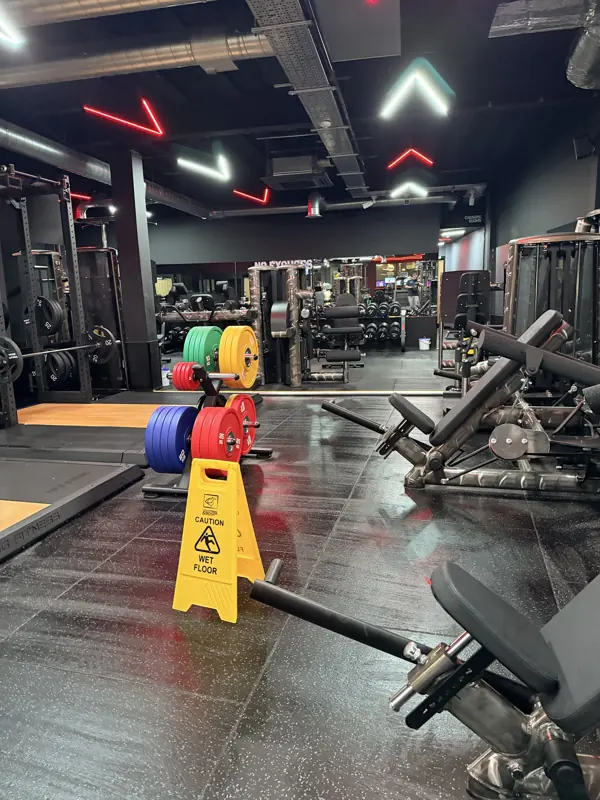 Gym floor with colourful weight plates and a wet floor sign